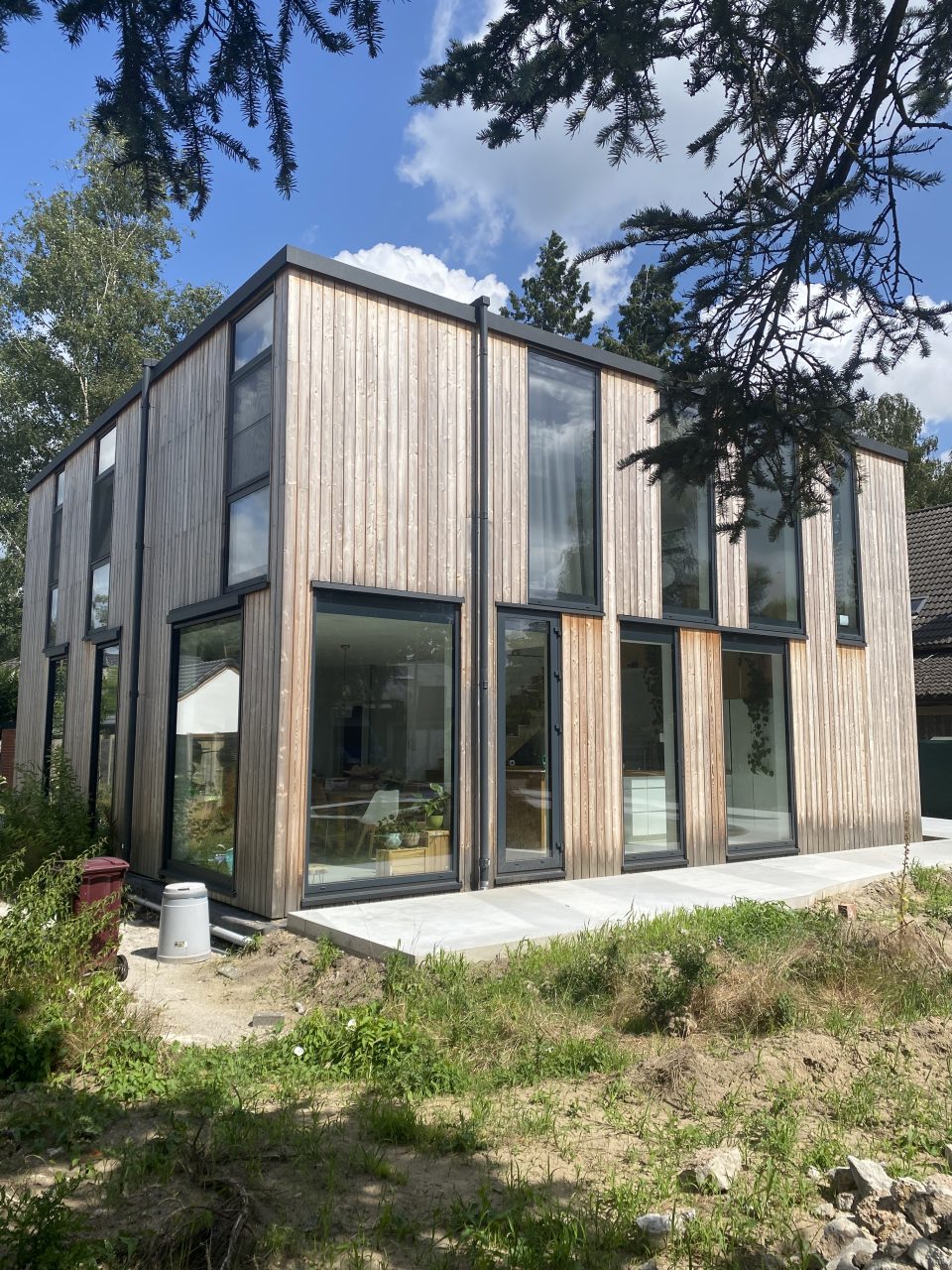 Three-quarter view of the timber-frame house in Belgium with full-height glazing facing the garden.