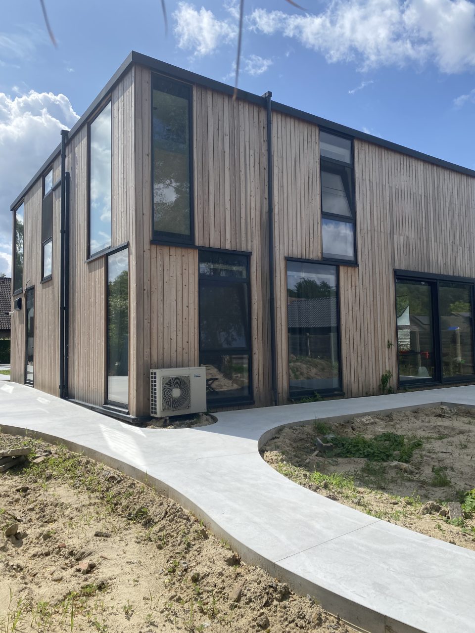 Front corner view of a modern timber-frame house in Belgium with vertical wooden cladding and tall windows.