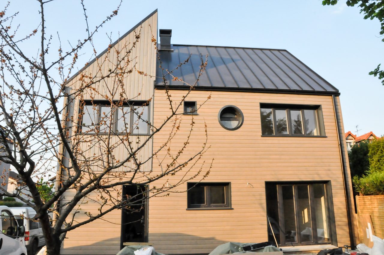 Contemporary timber home in France featuring mixed cladding, circular windows, and a metal roof.