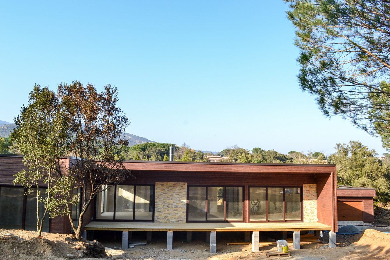 Front view of a single-storey timber-frame house in France with large windows and stone façade sections.
