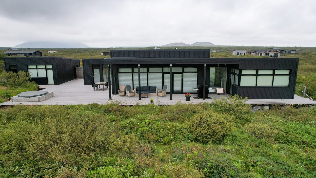 Front view of a contemporary Icelandic house surrounded by low vegetation with large glass doors.