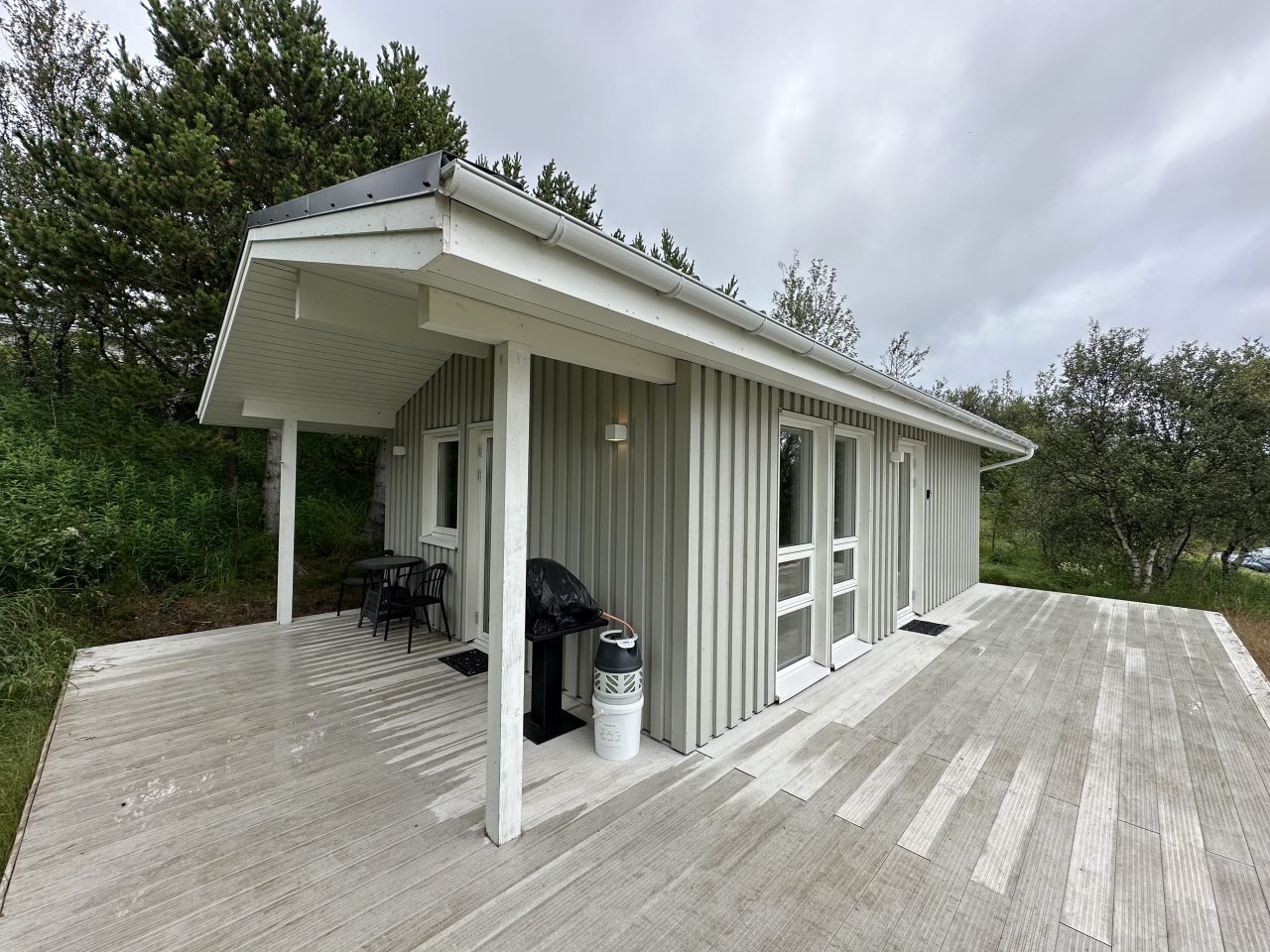Corner view of an Icelandic holiday cabin featuring light-grey cladding and an extended wooden terrace.