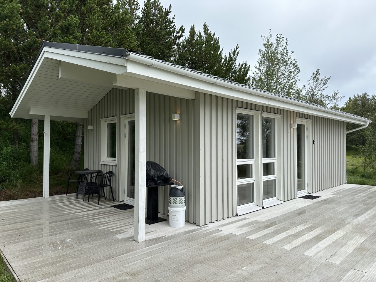 Side angle of a compact grey-clad cabin in Iceland with large windows and a timber deck.