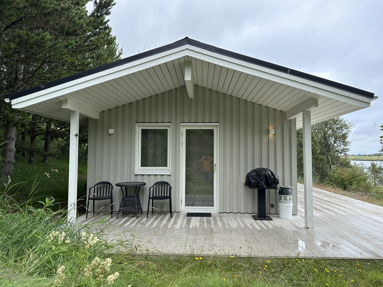Front view of a small Icelandic timber cabin with light-grey cladding and a covered entrance terrace.