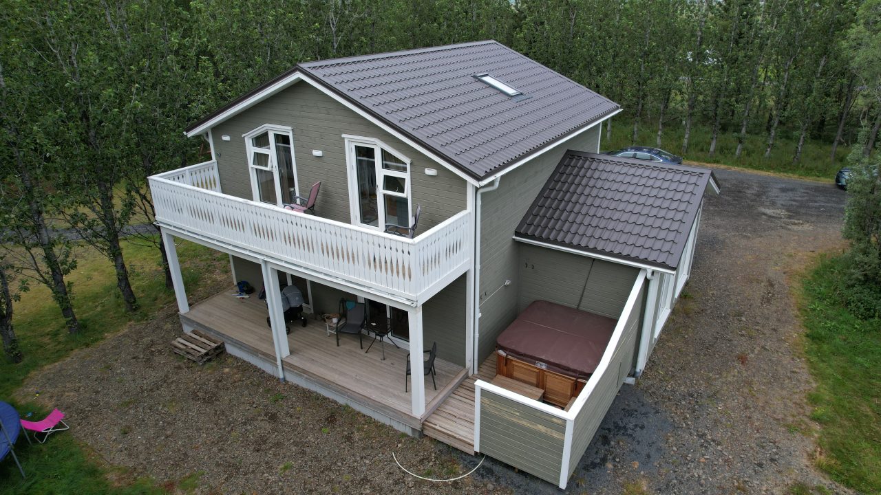 Aerial view of a two-storey timber house in Iceland with a balcony, terrace, and grey exterior cladding.