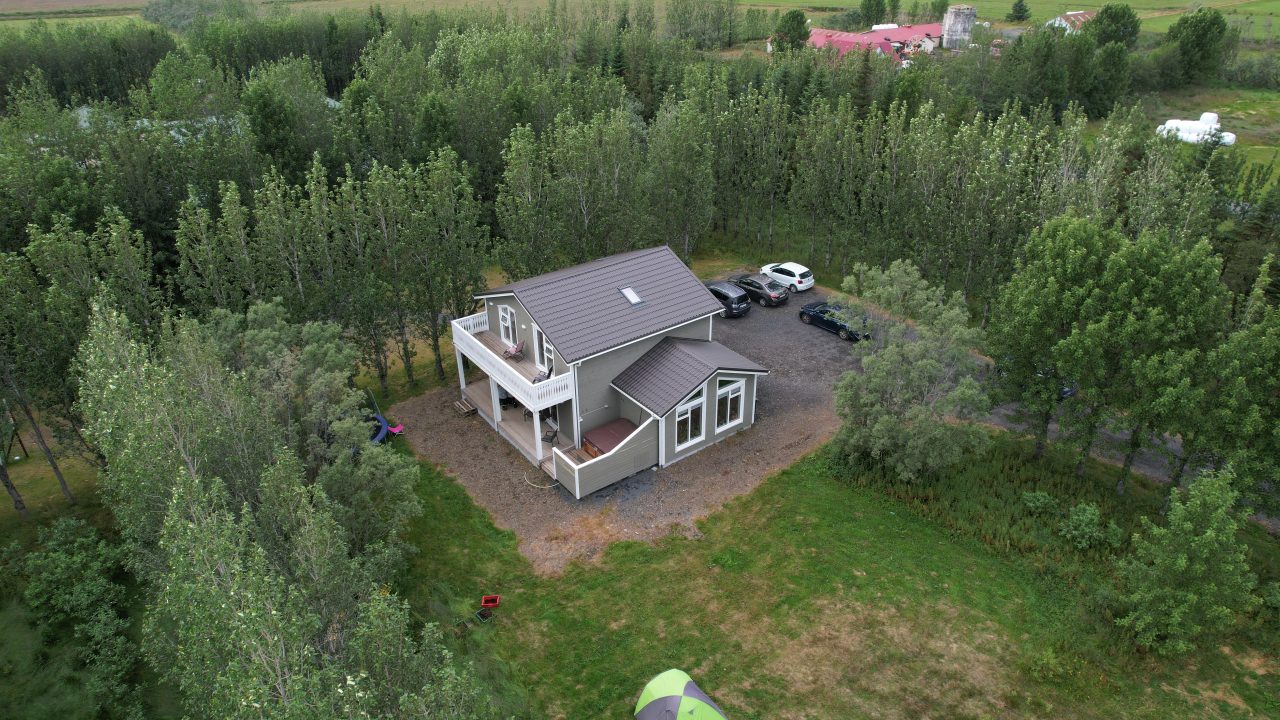Aerial view of a grey two-storey house surrounded by trees, showing the balcony, terrace, and parking area.