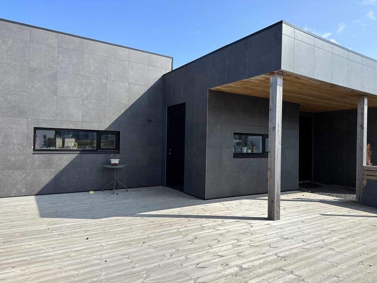 Modern Icelandic house with dark façade panels, recessed entrance, and a flat roof, viewed from the front terrace.