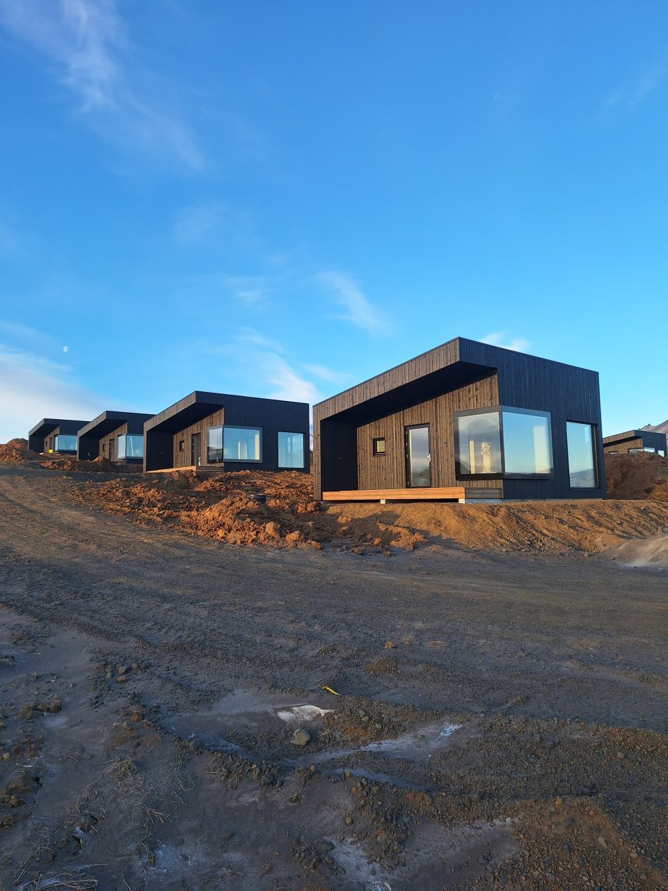 Black timber cabin units with large front windows arranged along a hillside.