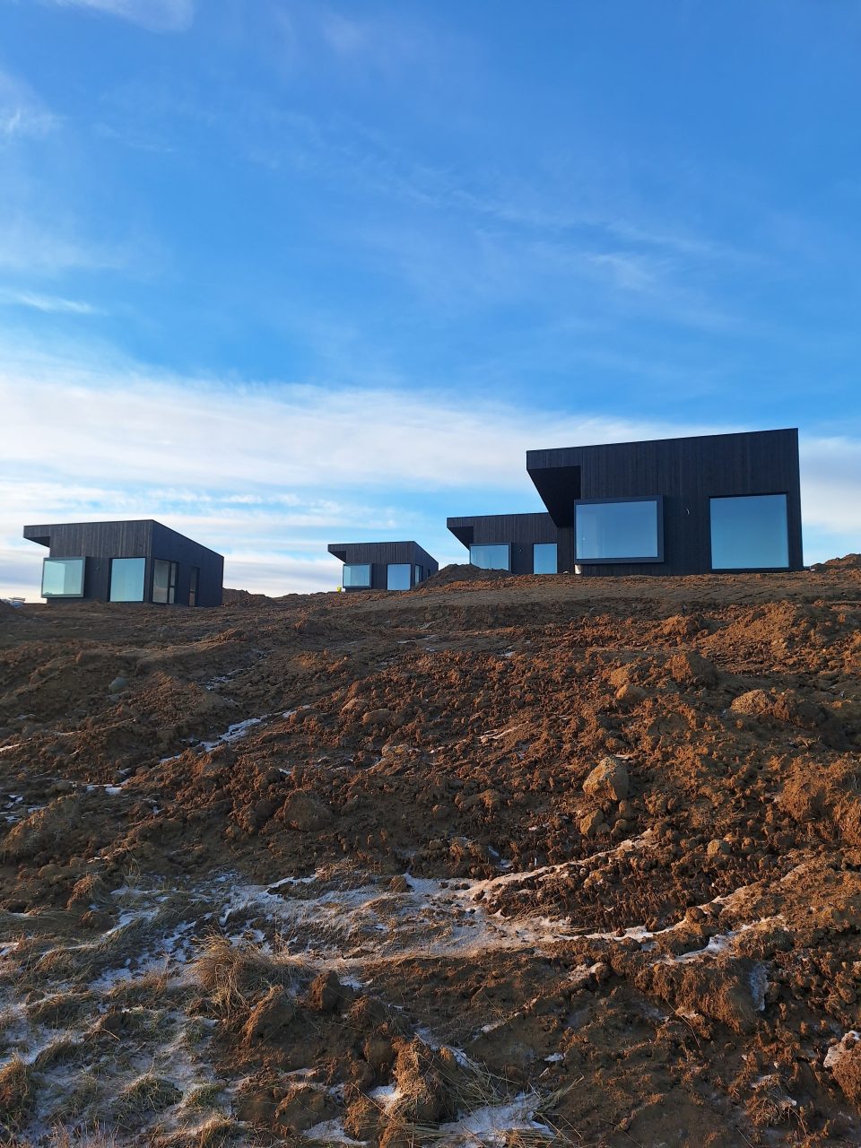 Row of black timber cabins positioned on a sloped construction site during winter.
