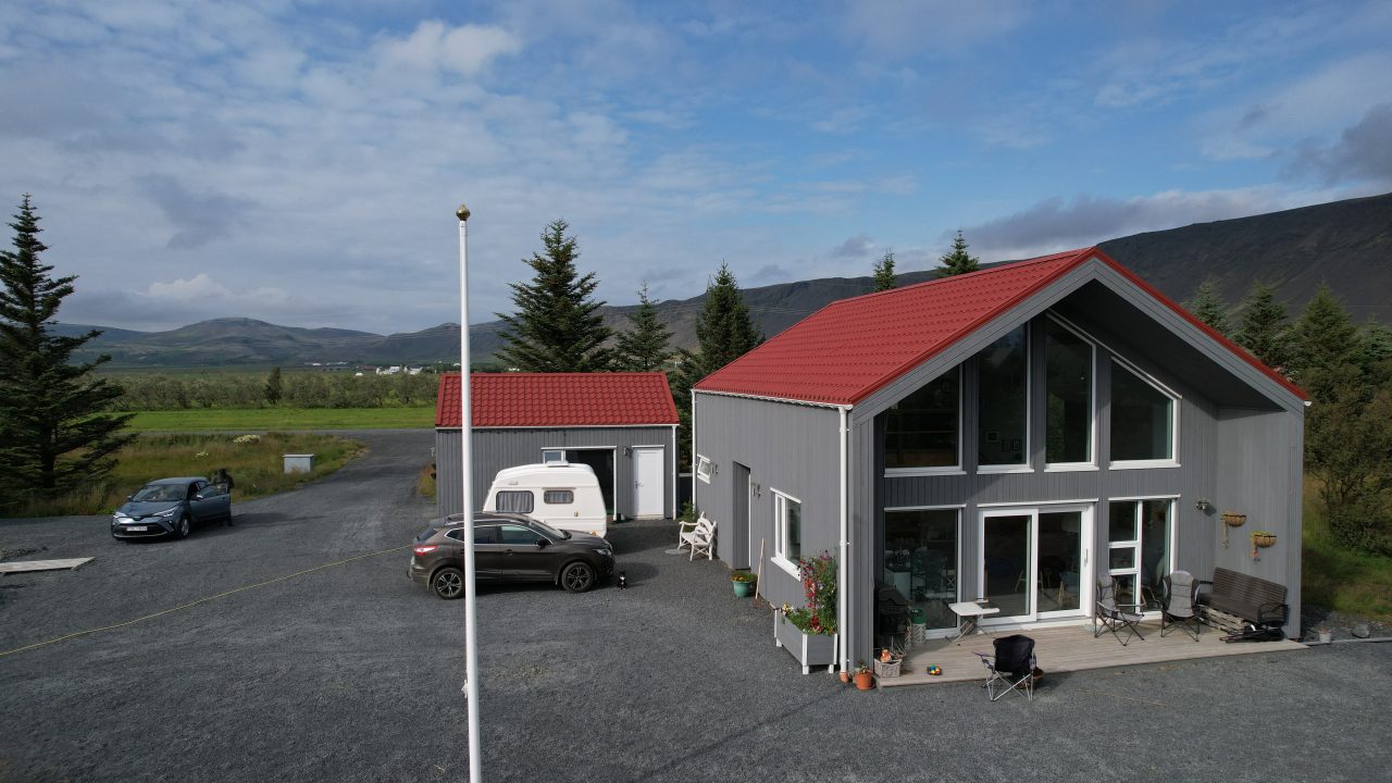 Barn-style VITA-84 house in Iceland with a red pitched roof and a separate outbuilding visible nearby.