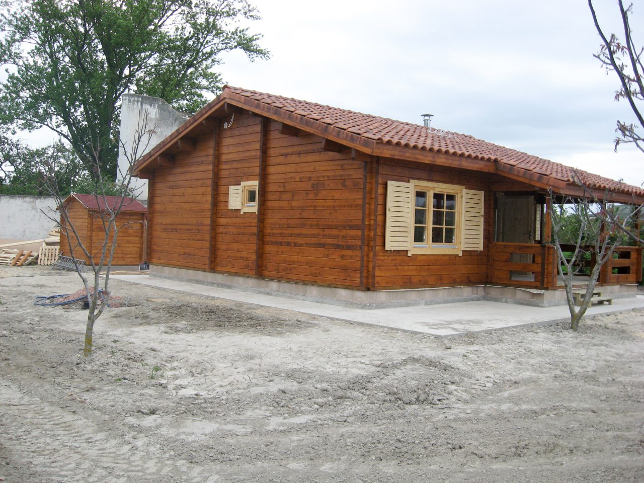 Single-storey timber cabin with tiled roof, extended eaves and a side window with shutters.