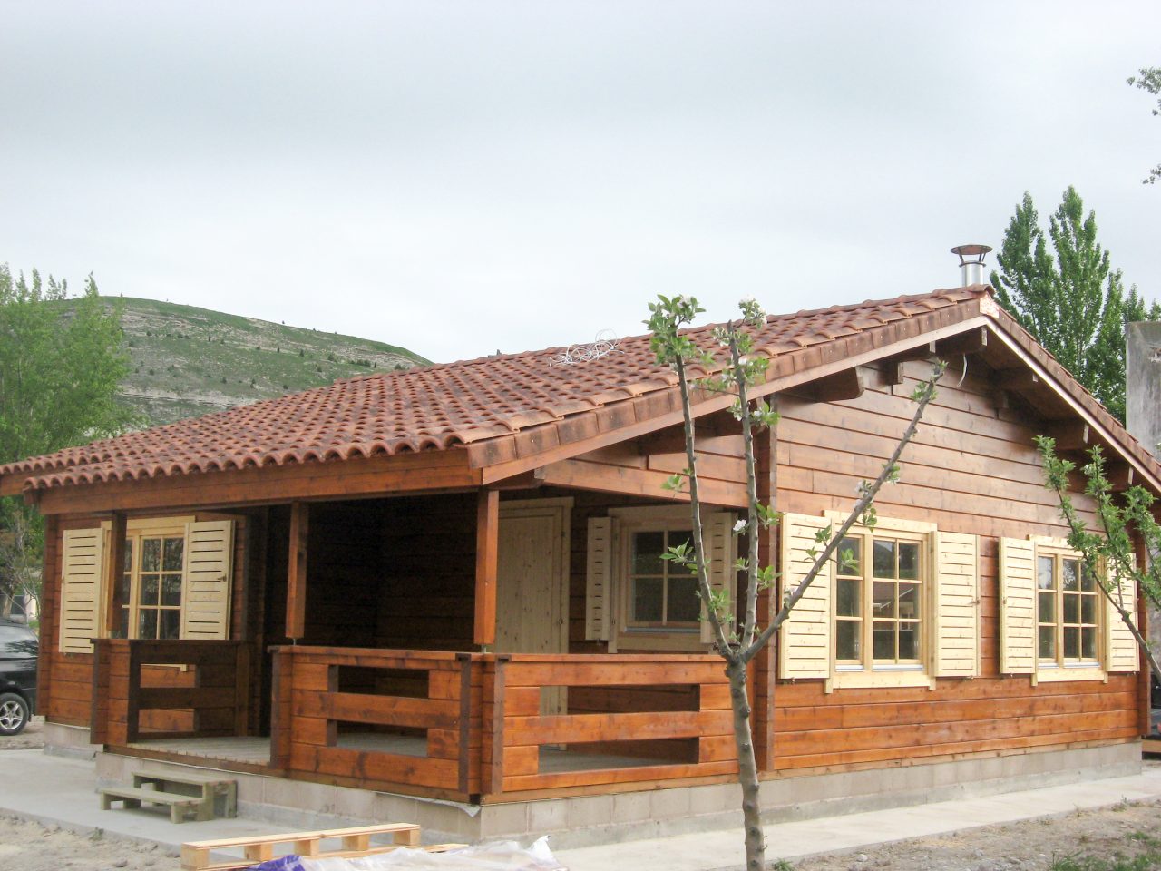 Wooden cabin with a covered veranda, corner posts and light-coloured window shutters.