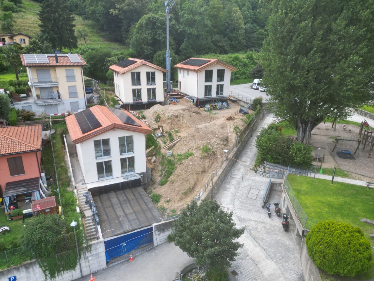 Three prefabricated houses on a Swiss hillside during site preparation.