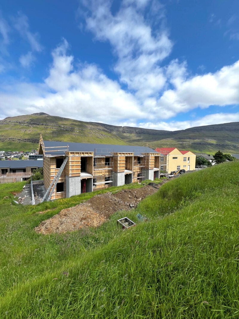 3-apartment timber-frame building under construction on a grassy hillside in the Faroe Islands.
