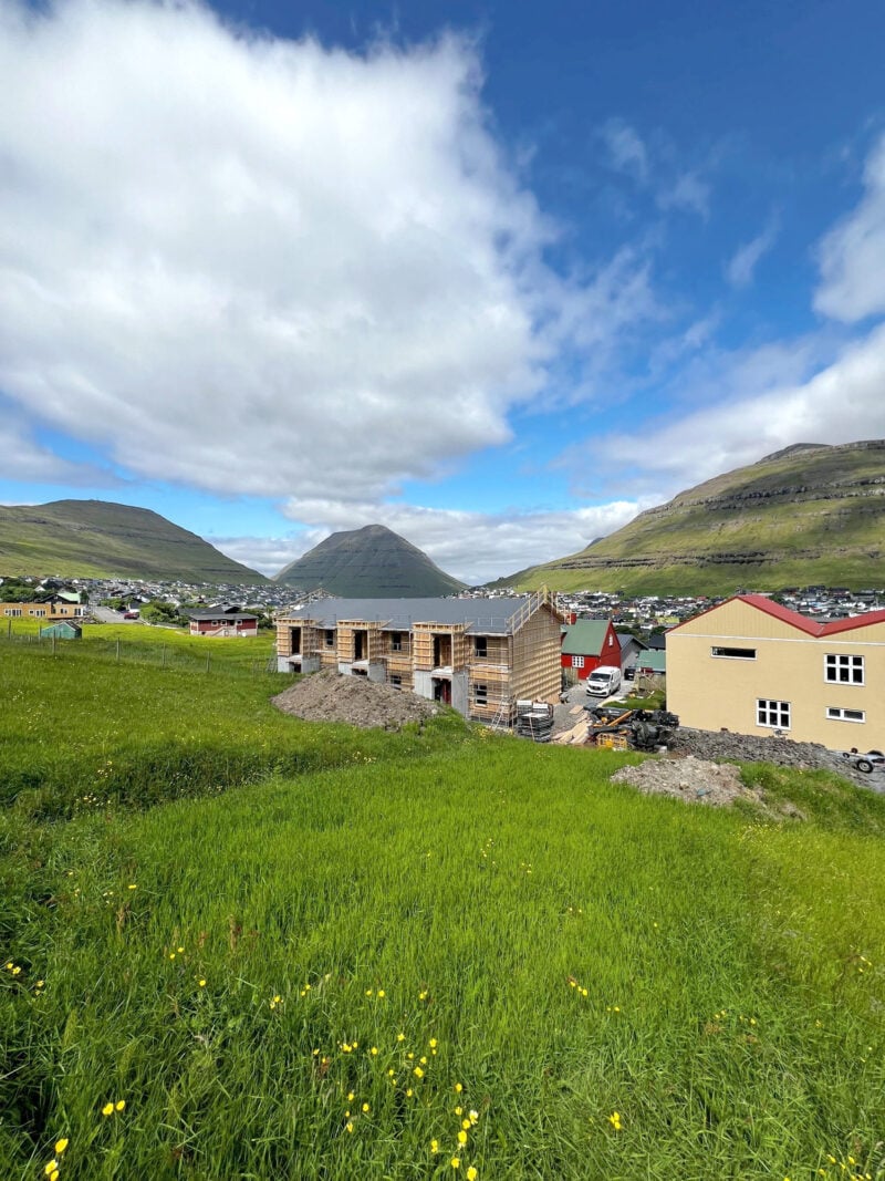 Prefabricated timber-frame 3-apartment building under construction in the Faroe Islands with mountains and cloudy sky.