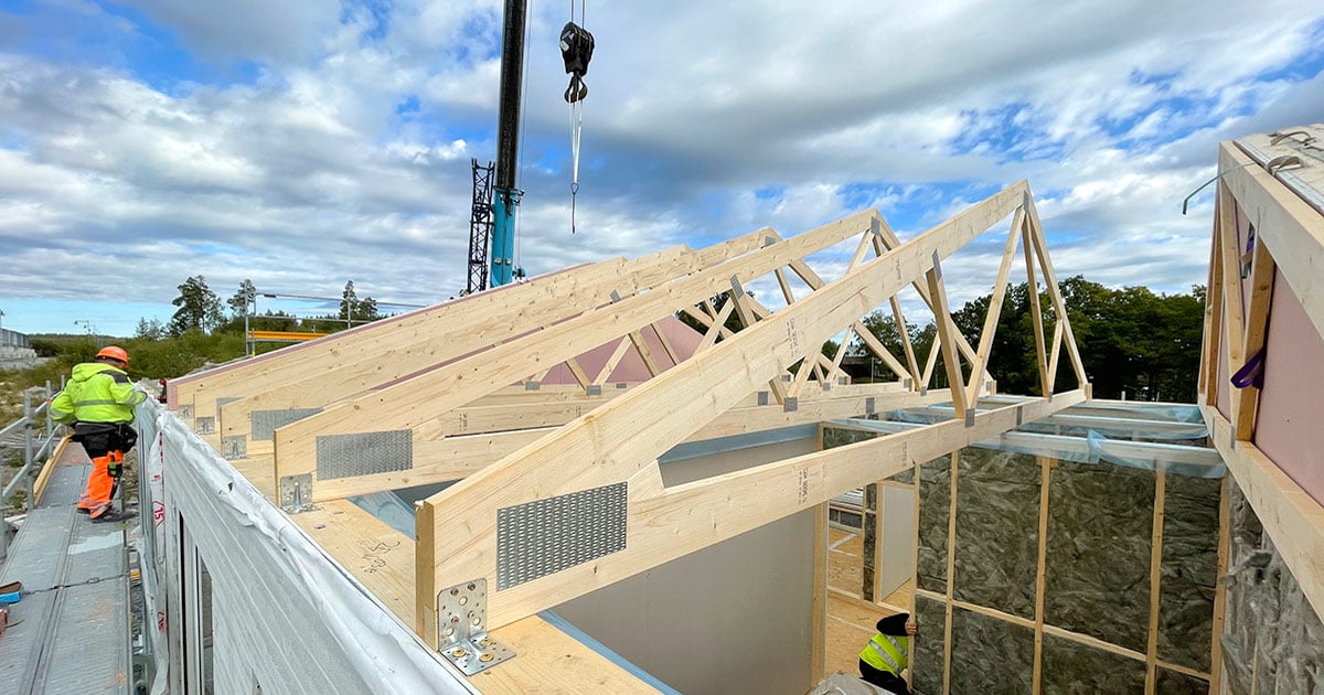 Prefabricated timber-frame roof trusses being installed by crane on a house construction site.