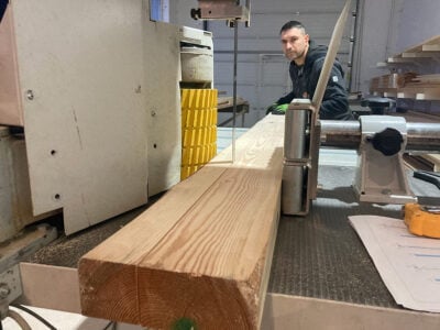 Worker cutting a timber beam on a woodworking machine in a factory.
