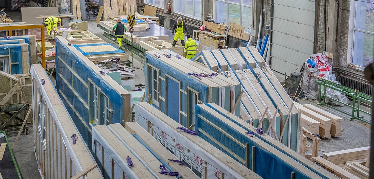 Prefabricated timber-frame wall panels with insulation and windows stored inside a factory.