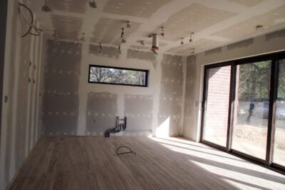 Interior room under construction with plasterboard walls, wiring, ventilation duct and large glass doors.