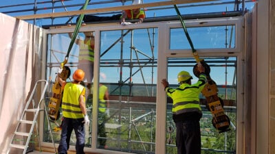 Workers installing large windows in a timber-frame house under construction.