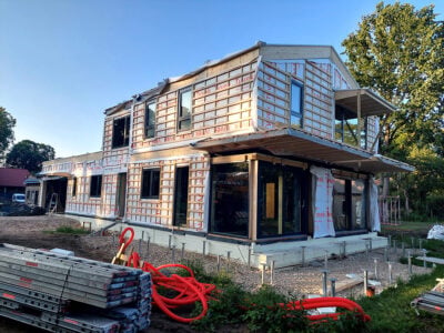 Two-storey timber-frame house under construction with weather membrane, windows and exterior battens.