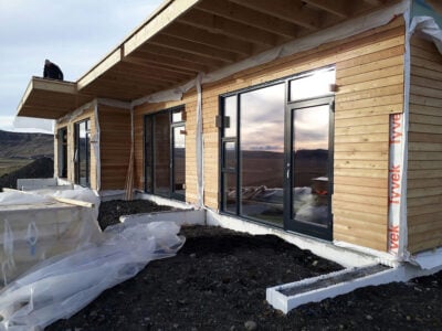Timber-frame house with wooden exterior cladding, large windows and roof overhang in Icelandic landscape.
