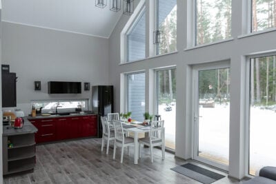 VITBŪVE VITA-83 standard design interior with kitchen, dining area and large windows facing a snowy forest.